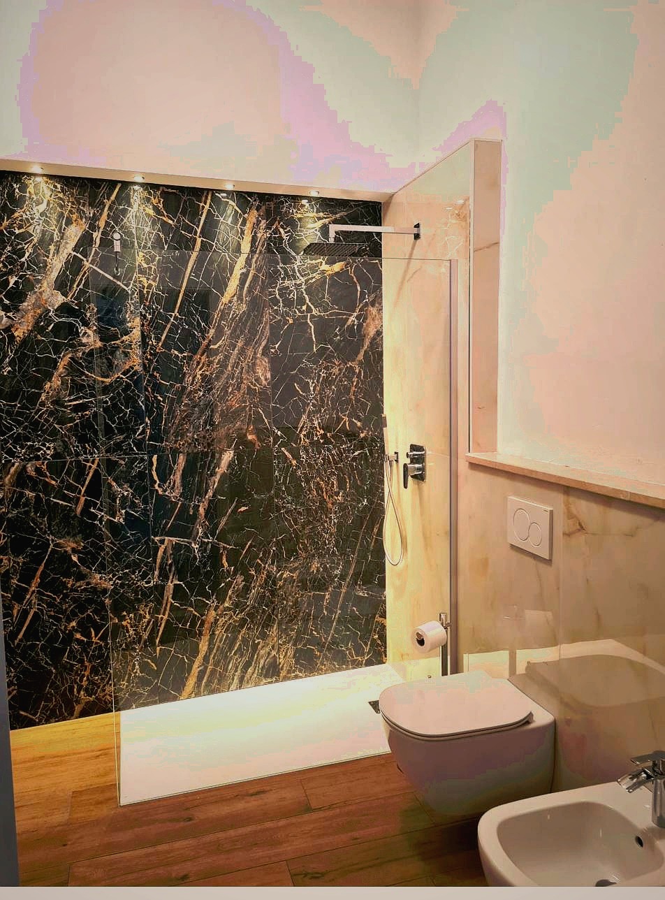 Luxury en suite bathroom at Corte Averaldo Lake Garda — dramatic black and gold marble walk-in shower, wooden floor, glass partition, bidet, San Felice del Benaco Italy
