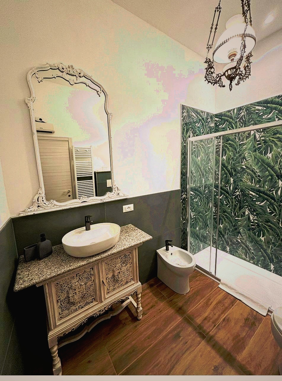 Boutique bathroom at Corte Averaldo holiday apartment — handpainted antique vanity unit, baroque white mirror, tropical botanical shower tiles, vintage pendant lamp, Lake Garda Italy